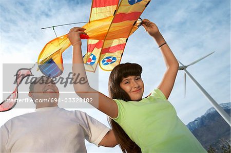Girl (7-9) holding airplane kite with father at wind farm