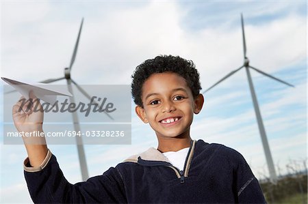 Boy (7-9) playing with paper plane at wind farm, portrait