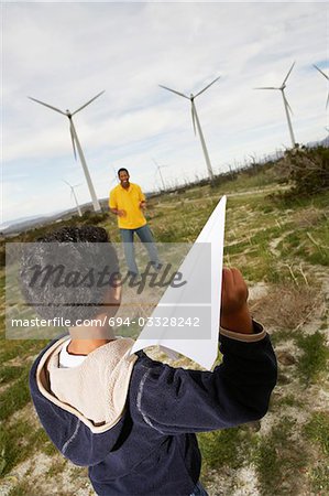 Father and son (7-9) playing with paper plane at wind farm
