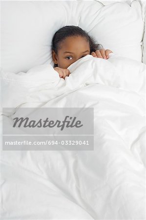 Girl (7-9) hiding under bed covers, portrait