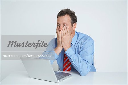 Studio shot of businessman with head in hands using laptop