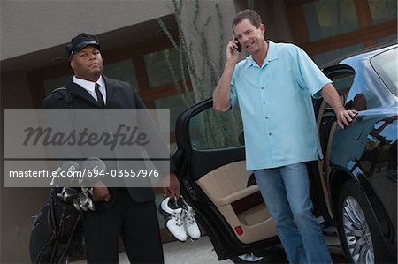 Chauffeur stands with golf equipment and owner of luxury vehicle