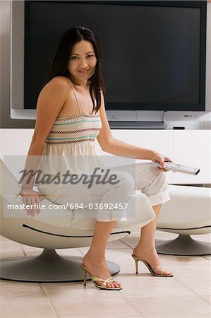 Woman with Remote Control sitting in front of large flat Screen Television, portrait