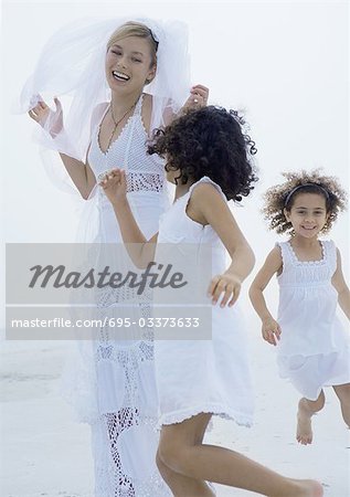 Two little girls running around bride on beach