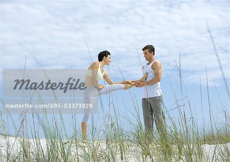 Man helping woman stretch leg on beach