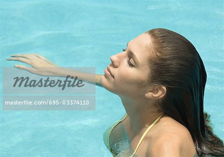 Woman standing in pool, head back and eyes closed, side view