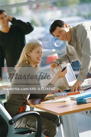 Office scene, man leaning toward female colleague, laughing