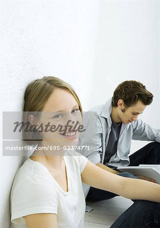 Teenage girl and young man sitting on floor, girl smiling at camera