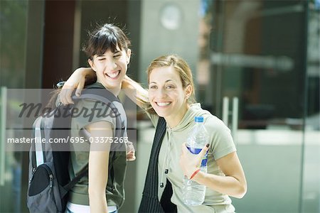 Two young women standing together, one with hand around other's shoulder, holding bottle of water