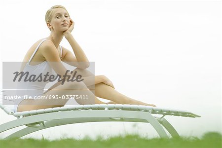Teenage girl sitting on lounge chair, holding head, looking at camera