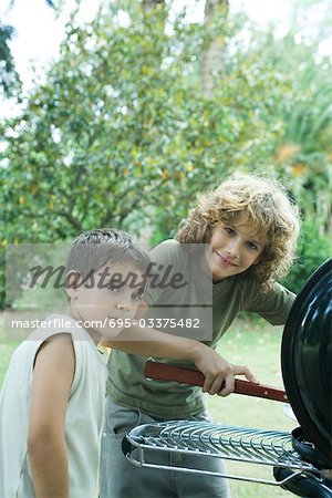 Two boys standing next to barbecue, looking at camera