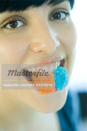 Woman holding pieces of candy between teeth, smiling at camera