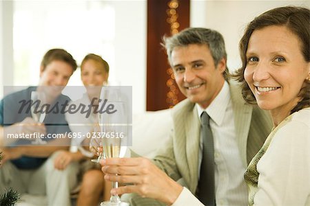 Couple making a toast with champagne, smiling at camera, friends in background