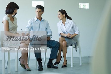 Three business associates sitting on chairs, holding documents on laps, talking