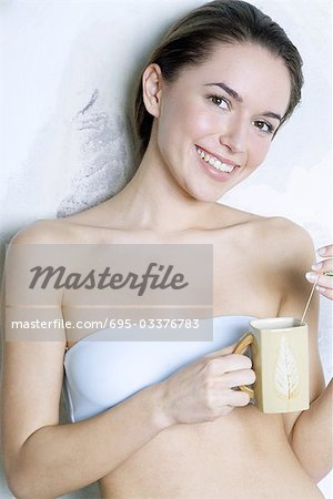 Young woman holding tea cup, smiling at camera, dressed in tubetop