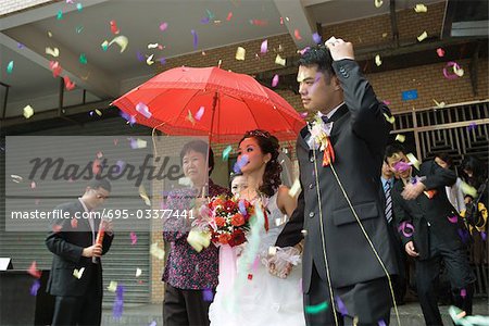 Chinese wedding, bride and groom leaving under confetti, bride covered by red parasol