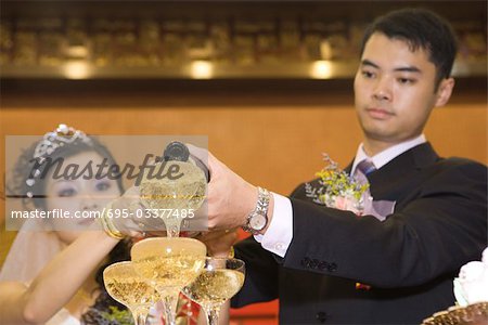 Bride and groom pouring champagne into stacked champagne glasses together