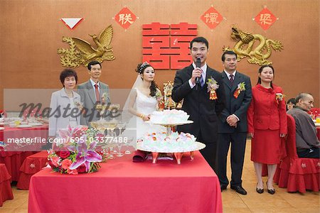 Groom standing in front of bride and parents, speaking into microphone