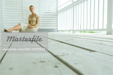 Woman sitting on deck, focus on wooden planks, surface level view