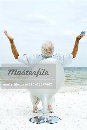 Senior man holding cell phone, arms up and head back, rear view