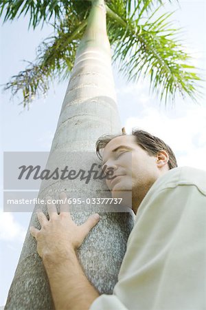 Man embracing tree, eyes closed, low angle view