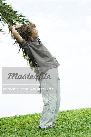 Boy leaning against palm branch, side view