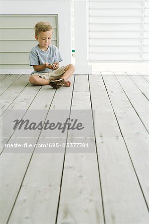 Boy sitting on the ground next to bird's nest, looking down at eggs in his hands