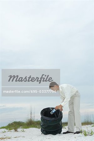 Man at the beach, placing water bottle in garbage can