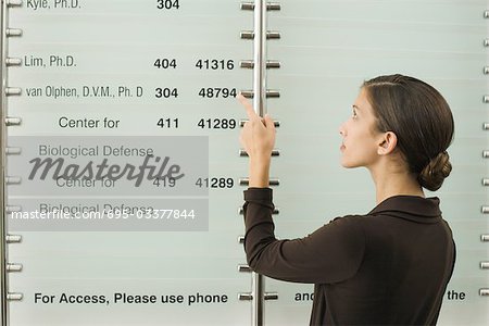 Teenage girl looking at building directory, pointing at number with finger