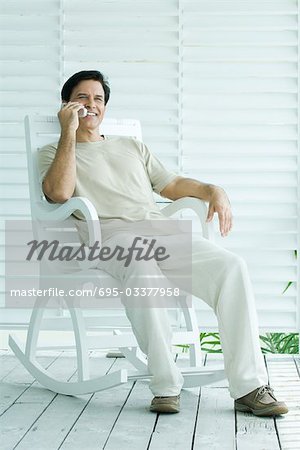 Man sitting in rocking chair, using cell phone, full length