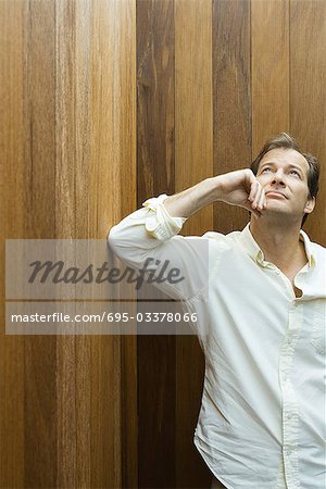 Man leaning elbow against wall, holding chin, looking up