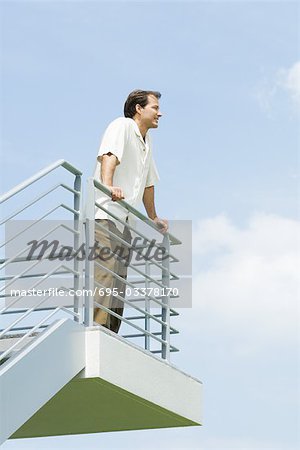 Man leaning against railing, looking into distance, low angle view