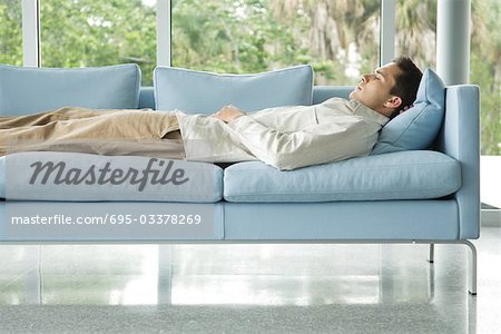 Man lying on couch with hand behind head, eyes closed, side view