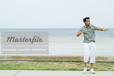 Man listening to headphones at the beach, dancing, looking away