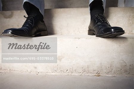 Businessman sitting on steps, cropped view of feet, low angle view