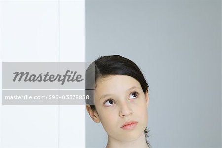 Preteen girl leaning against wall, looking up