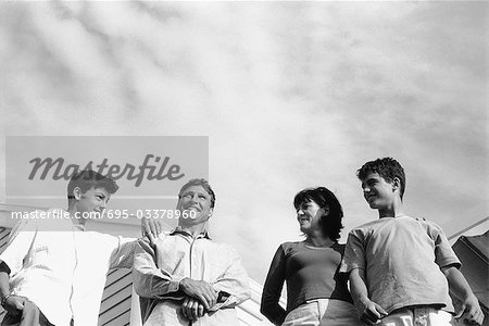 Family standing side by side outdoors, smiling, man looking up