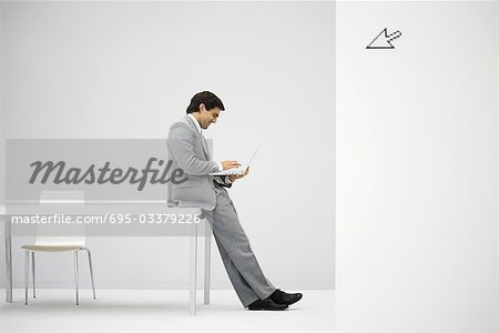Businessman leaning against desk, using laptop computer, cursor graphic in foreground