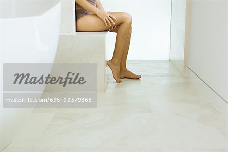 Woman sitting in bathroom, in underwear, low section