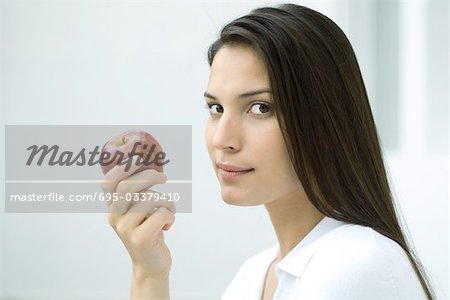 Woman holding apple, looking sideways at camera