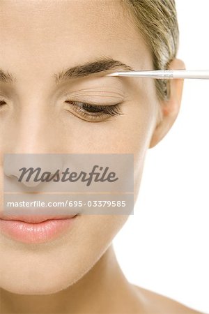 Woman applying eye make-up, looking down, cropped view