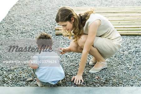 Mother and toddler crouching on gravel, looking at rocks