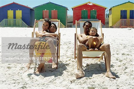 Family at the beach, parents sitting in deckchairs and holding children on their laps