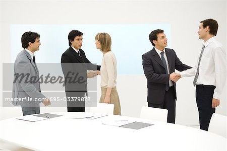 Group of professionals standing beside table, smiling, some shaking hands