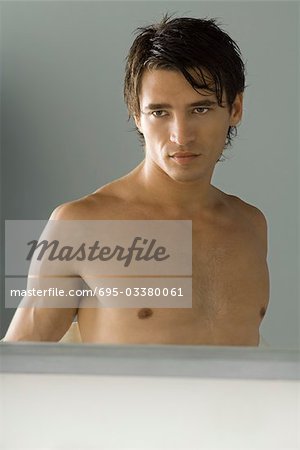 Bare-chested man looking at self in mirror, cropped view of reflection