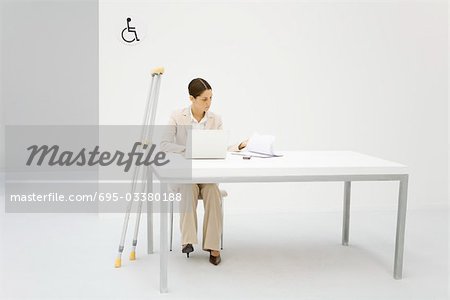 Professional woman working in office, crutches leaning against desk beside her