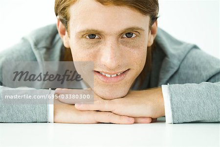 Young man resting head on folded arms, smiling at camera, portrait