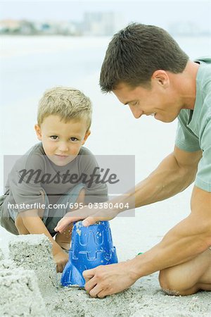 Man making a sand castle with young son