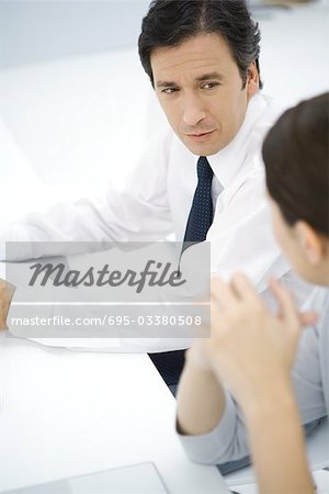 Professional man sitting at desk, talking with female colleague, high angle view