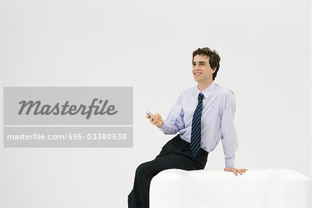 Young male professional sitting on armchair, holding cell phone, smiling